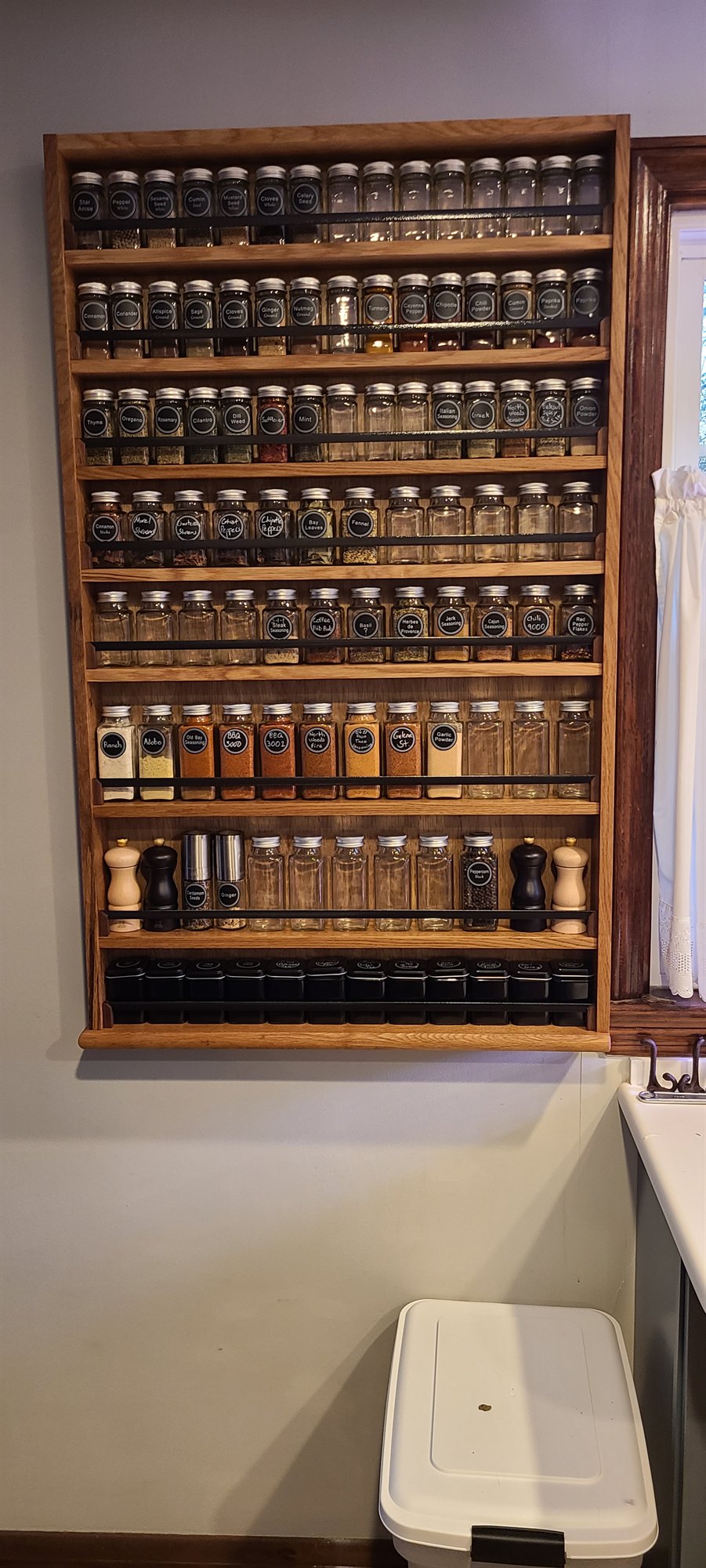 Custom oak wall-mounted spice rack filled with rows of labeled glass jars